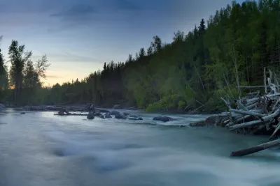 A long-exposure shot of a rushing Alaskan river at twilight, with smooth water flowing over dark rocks.